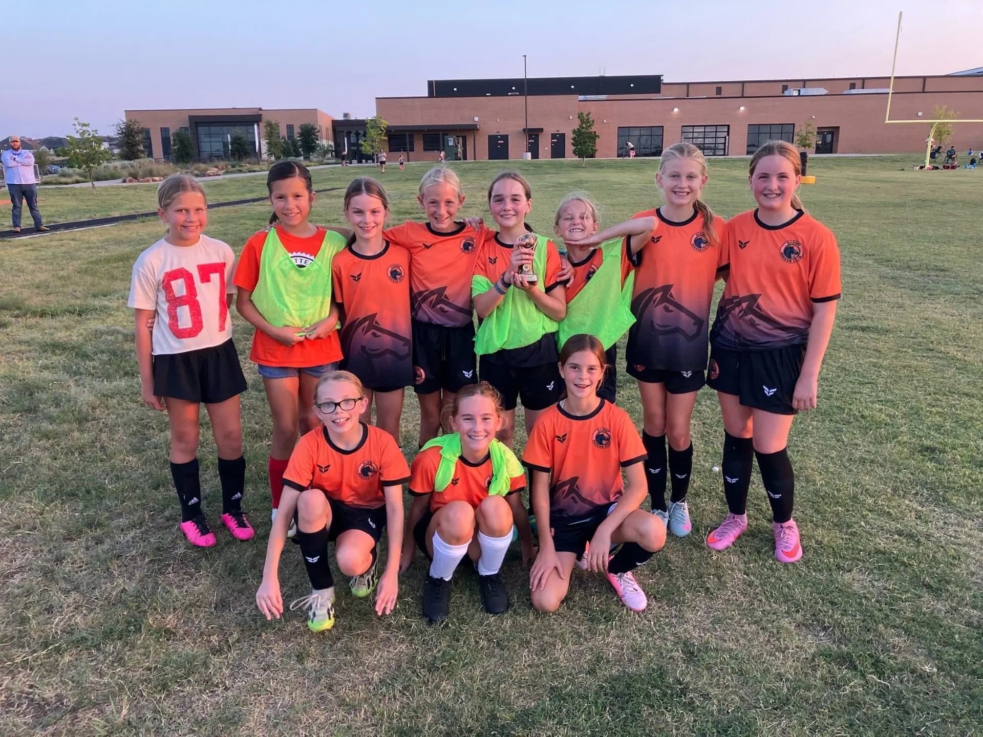 A young Aledo Soccer Club girls team in their orange kits smiling together after training