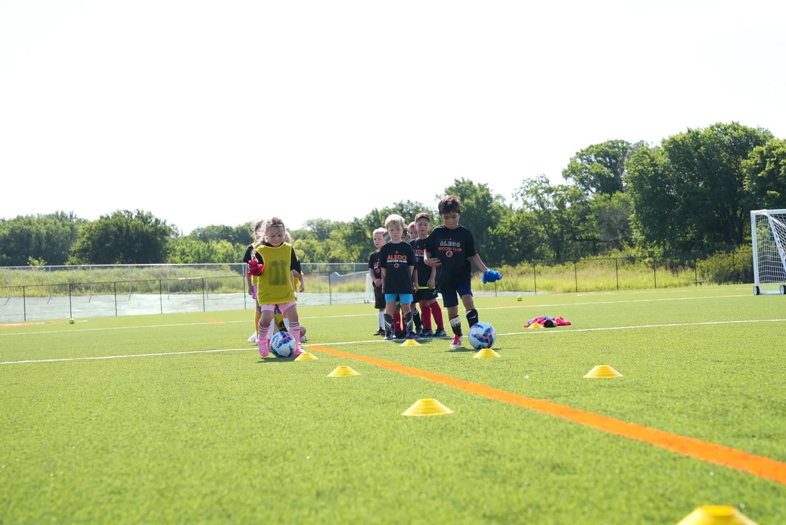 Young Aledo players lining up to dribble through cones during a training session