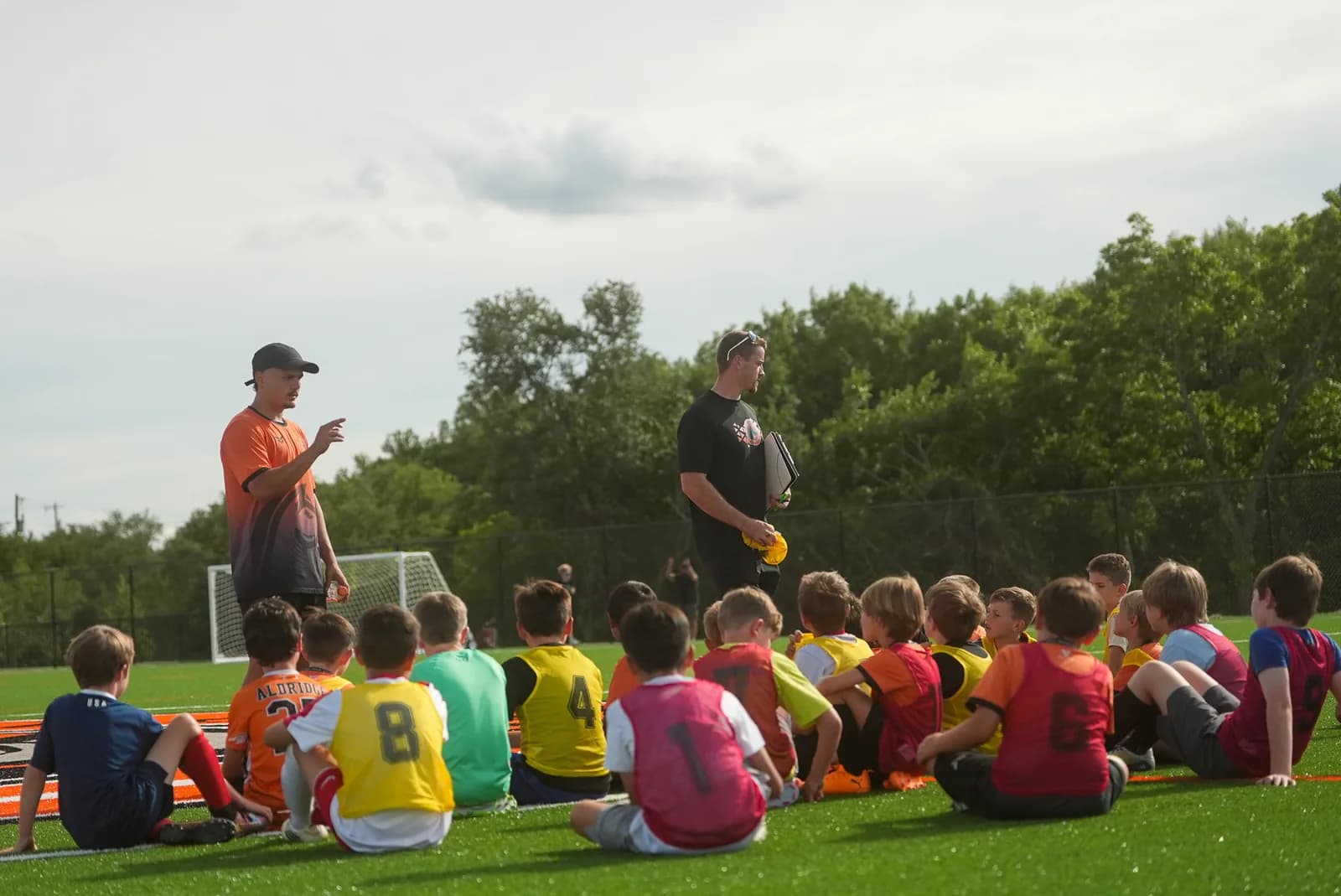 Two Aledo Soccer Club coaches leading a team talk with young players on the pitch