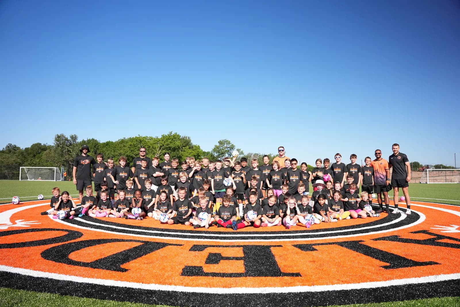 Aledo Soccer Club campers celebrating together on the crest at the center circle of The Stable